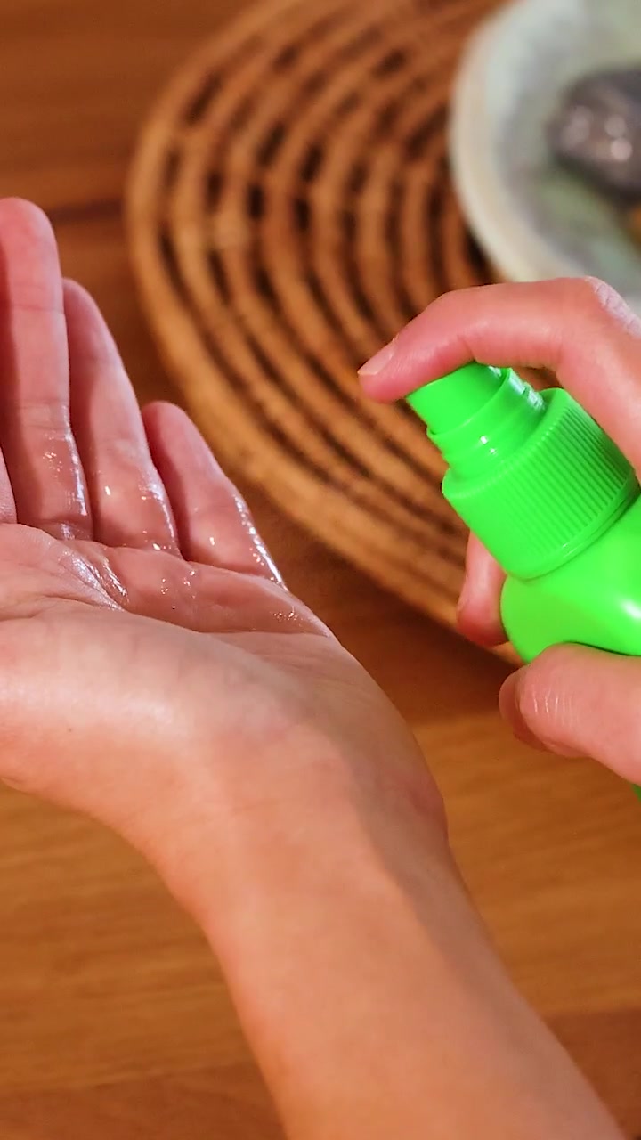 Mani che usano uno spruzzino verde per applicare disinfettante su una superficie di legno con illuminazione naturale