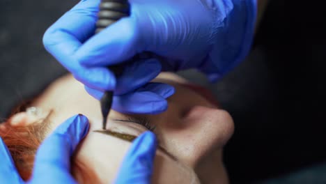 procedure of eyebrow tattoo with using a needle for applying a dye in a beauty salon. cosmetology. beauty industry