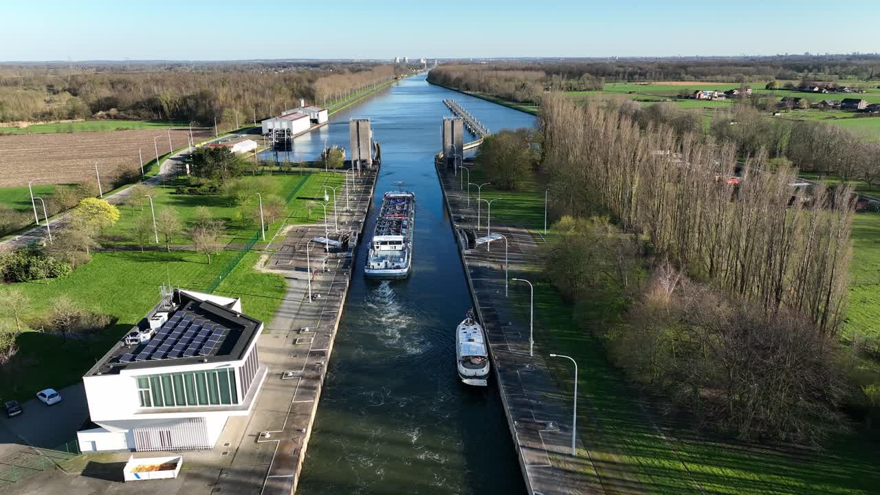 Fixed aerial camera view of Antwerp canal lock with cargo and passenger ships crossing through the waterway on a clear sunny day