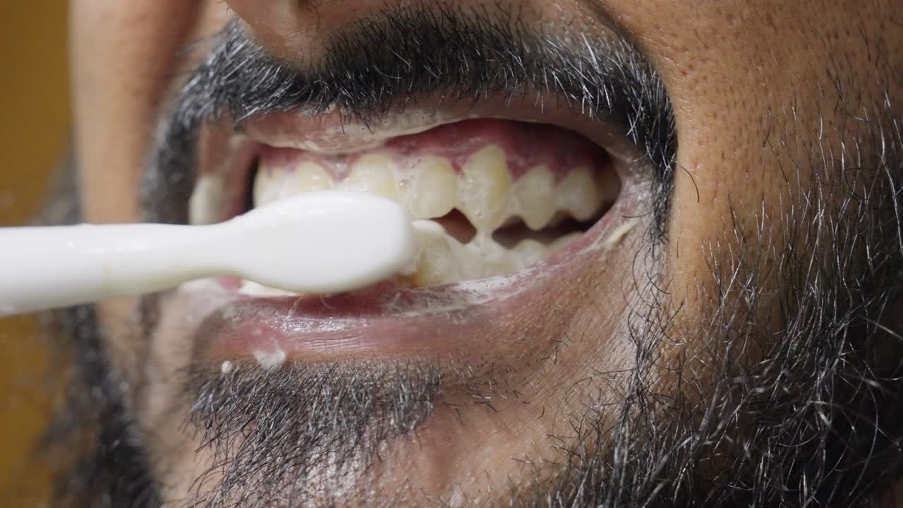 A slow-motion, close-up footage of a South Asian man brushing his teeth, with a blurred background. Dental care and hygiene concept