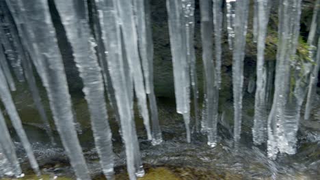 Schwenkaufnahme-Eines-Fließenden-Baches-Unter-Eiszapfen-In-Der-Natur-Der-Schweiz