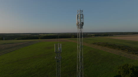 Dos-Torres-Celulares-En-Medio-De-Tierras-De-Cultivo-Durante-El-Amanecer,-Orbital-Aérea