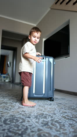 caucasian toddler approaches a camera pulling a big suitcase. going to vacation. low angle view. vertical video.