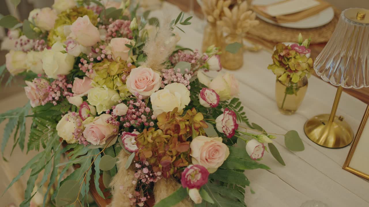 Exuberante centro de mesa nupcial con rosas rosadas, ranúnculos, hortensias y eucalipto sobre una mesa.
