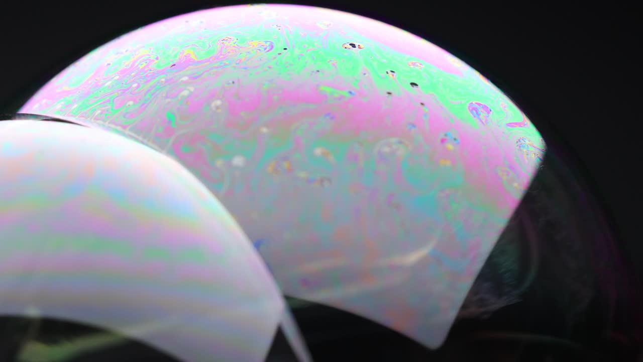 Vibrant soap bubble displays shifting colors and reflections against a dark background, showcasing dynamic light and fluid movement