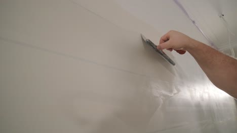 man plastering the walls with finishing putty in room with putty spatula