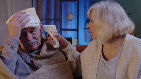 senior couple measures temperature with contactless digital thermometer during coronavirus lockdown