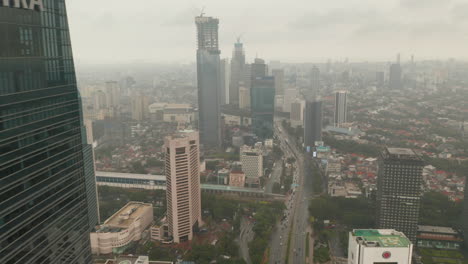 La-Vista-Aérea-Revela-Volar-Desde-Detrás-De-Un-Rascacielos-Hasta-Una-Vista-Amplia-Del-Horizonte-De-La-Ciudad-De-Yakarta-En-Un-Clima-Nublado