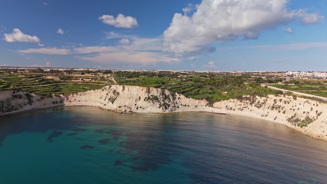 Orbitaalinen drone-näkymä Triq Xrobb L-Għaġinin lahden yllä paljastaa turkoosit Välimeren vedet, korkeat kalkkikivikalliot ja vihreän talvisen rannikkomaiseman Etelä-Maltalla kirkkaan sinisen taivaan alla.