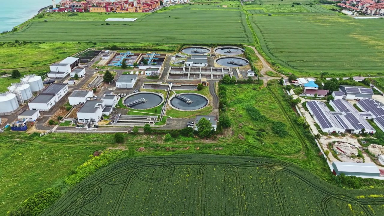Wastewater treatment facility located in a rural area surrounded by green fields and residential buildings during daytime hours