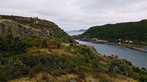 A drone sweeps over the St John&#039;s Battery&#039;s rugged cliffside, capturing a stormy sky and the harbour below, with dramatic rocky slopes and dark green foliage