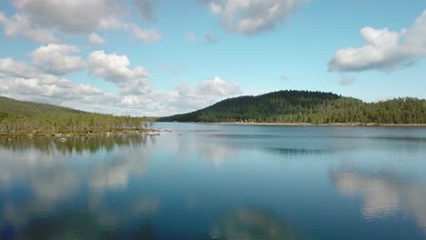 forward low altitude aerial shot over a calm lake in finland with clouds reflected in it