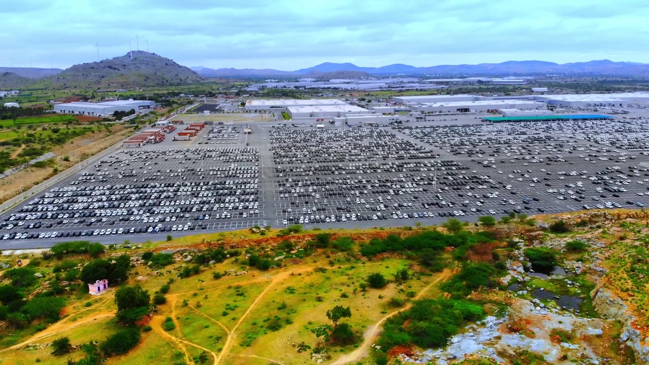 Vista superior de estacionamento de armazém de carros novos em fábrica gigante, com longas filas de automóveis coloridos prontos para venda, incluindo um novo Kia.