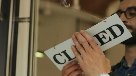 close-up view of young man turning over a closed" signboard in coffee shop door"