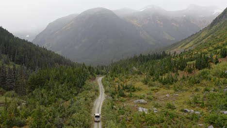 aerial following vehicle driving dirt road through british columbia mountains