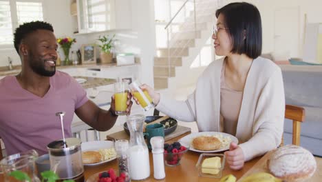 pareja feliz y diversa sentada a la mesa y desayunando