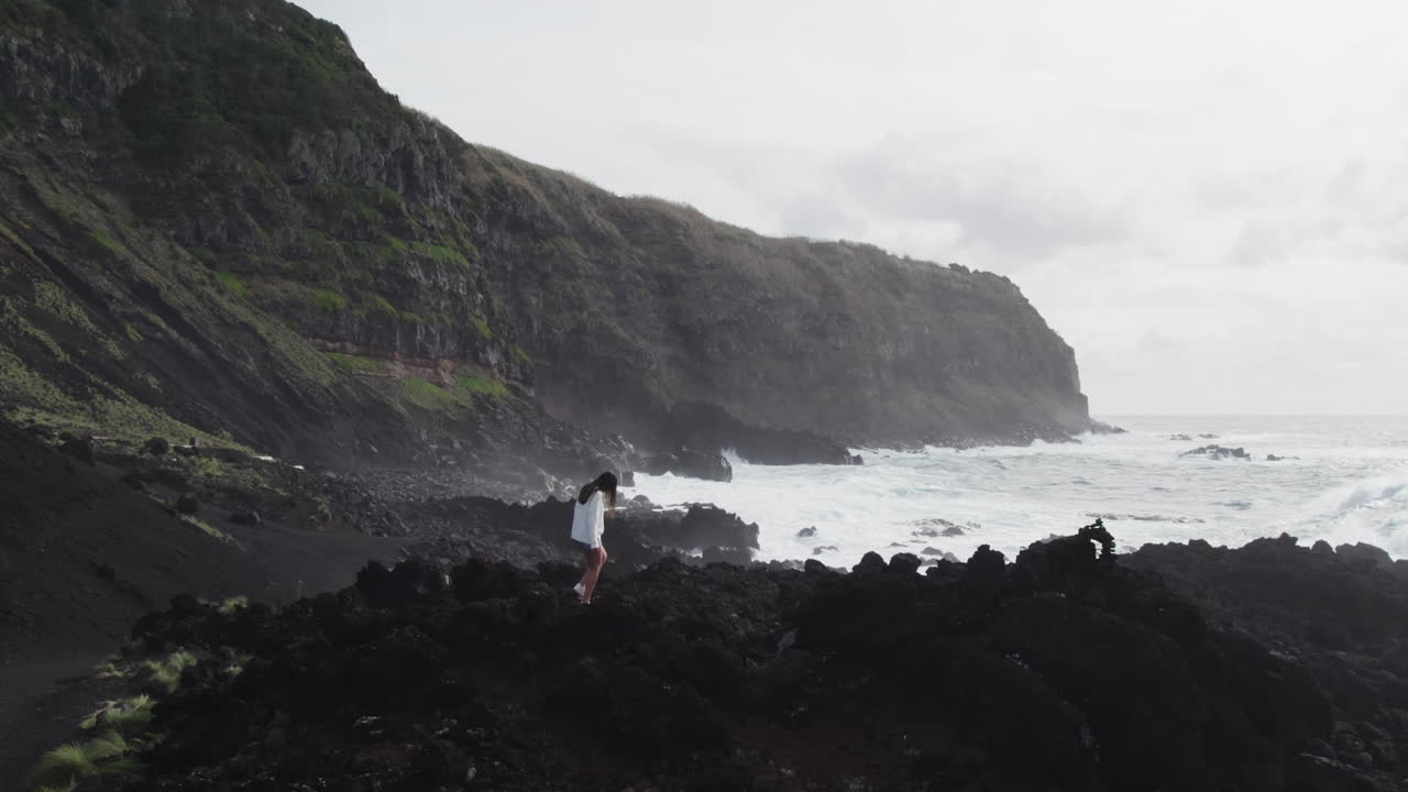 mujer por la costa rocosa, azores, ponta da ferraria olas que se estrellan