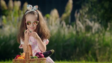 A-cute-child-is-sitting-on-the-lawn-near-a-basket-of-vegetables.-Picnic-concept