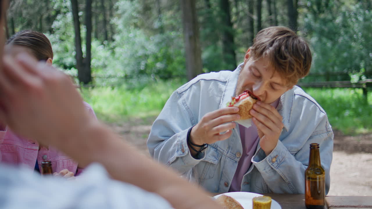 Friends eating burgers picnic in sunny forest closeup. Guy adding ketchup food