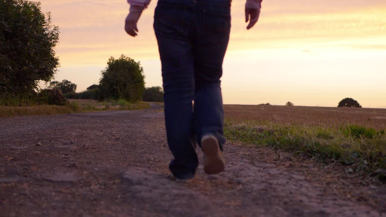 mujer caminando hacia la puesta de sol en un camino polvoriento y seco de cerca