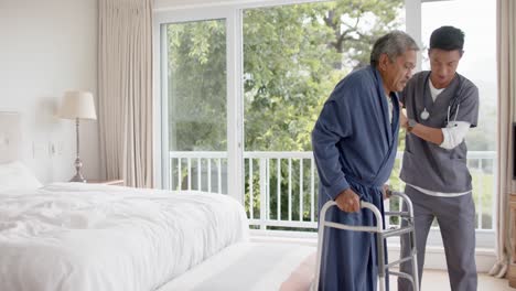 médico varón diverso ayudando a un paciente varón anciano usando un marco para caminar en casa, cámara lenta