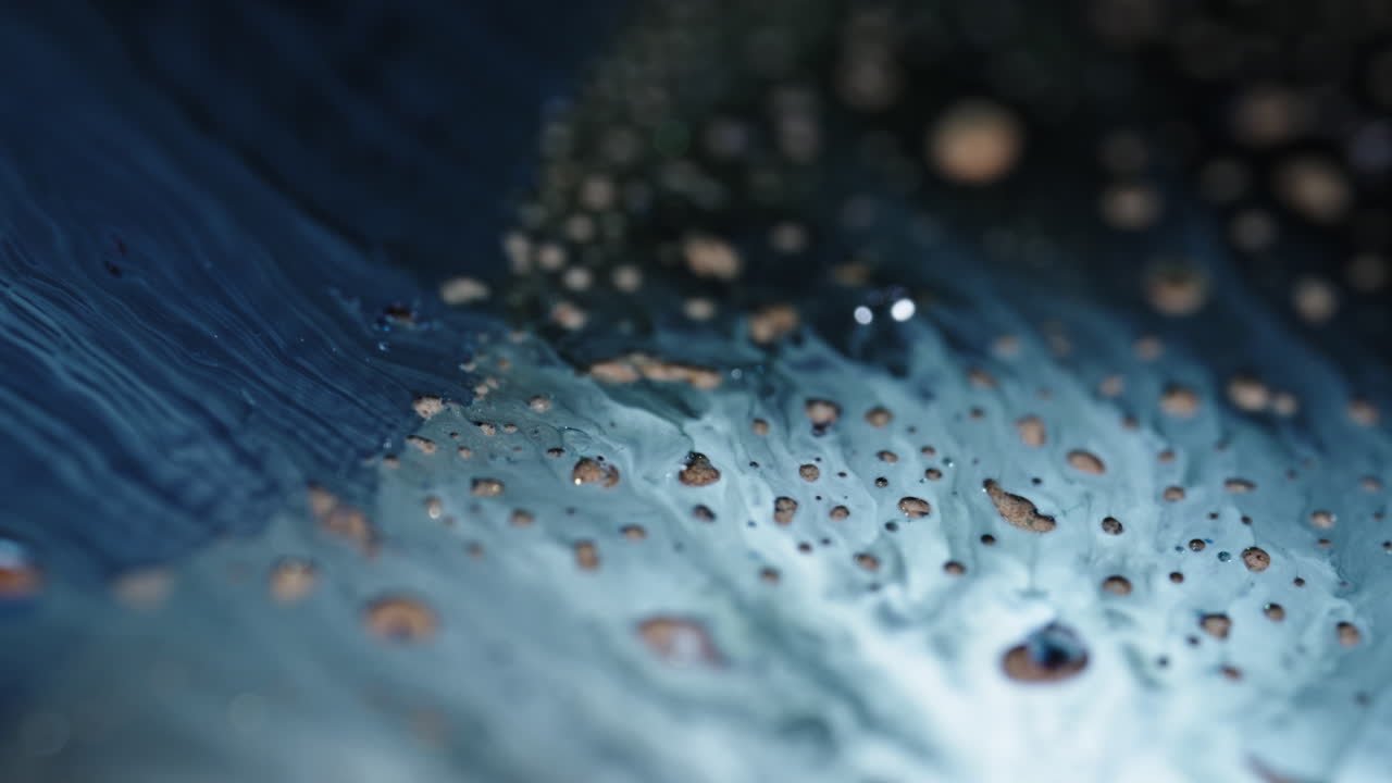 Blue and white liquids mix and form abstract patterns in a close-up macro view, creating a fluid texture
