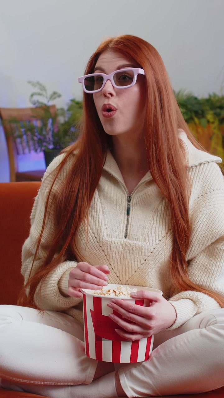 Donna seduta sul divano a mangiare popcorn e guardare interessanti TV 3D film sport gioco online a casa
