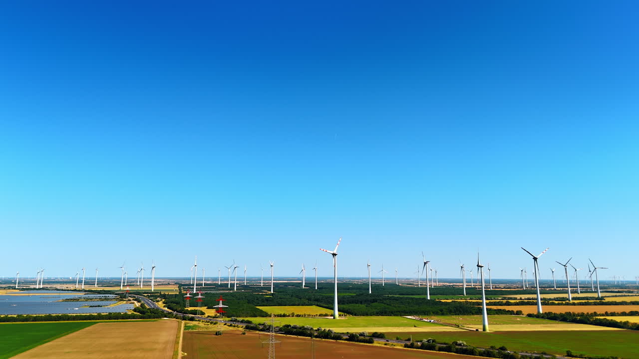 Turbines produce energy in fields. Wide view of wind turbines spinning in agricultural fields under a clear blue sky during daytime