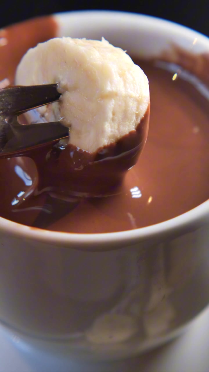 Primer plano de una rodaja de plátano sumergida en fondue de chocolate derretido