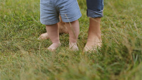 close-up dos pés descalços do bebê e da mãe dando os primeiros passos na grama verde