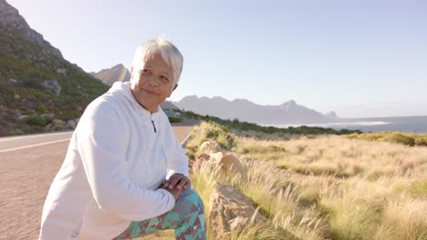 Happy-senior-biracial-woman-stretching-in-mountains-on-sunny-day,-in-slow-motion