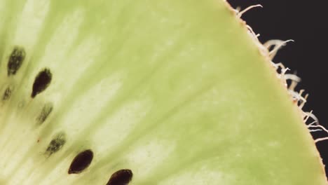 Micro-video-of-close-up-of-kiwi-fruit-slice-with-copy-space-on-black-background