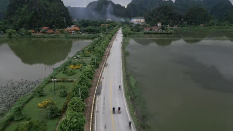 Coole-Luftaufnahme,-Die-Menschen-Auf-Fahrrädern-Auf-Einer-Asiatischen-Straße-Folgte,-Erklang-Mein-Wasser-Und-Atemberaubende-Grüne-Berge