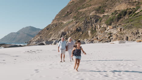 multi generation family meeting as they walk along sandy beach on summer vacation