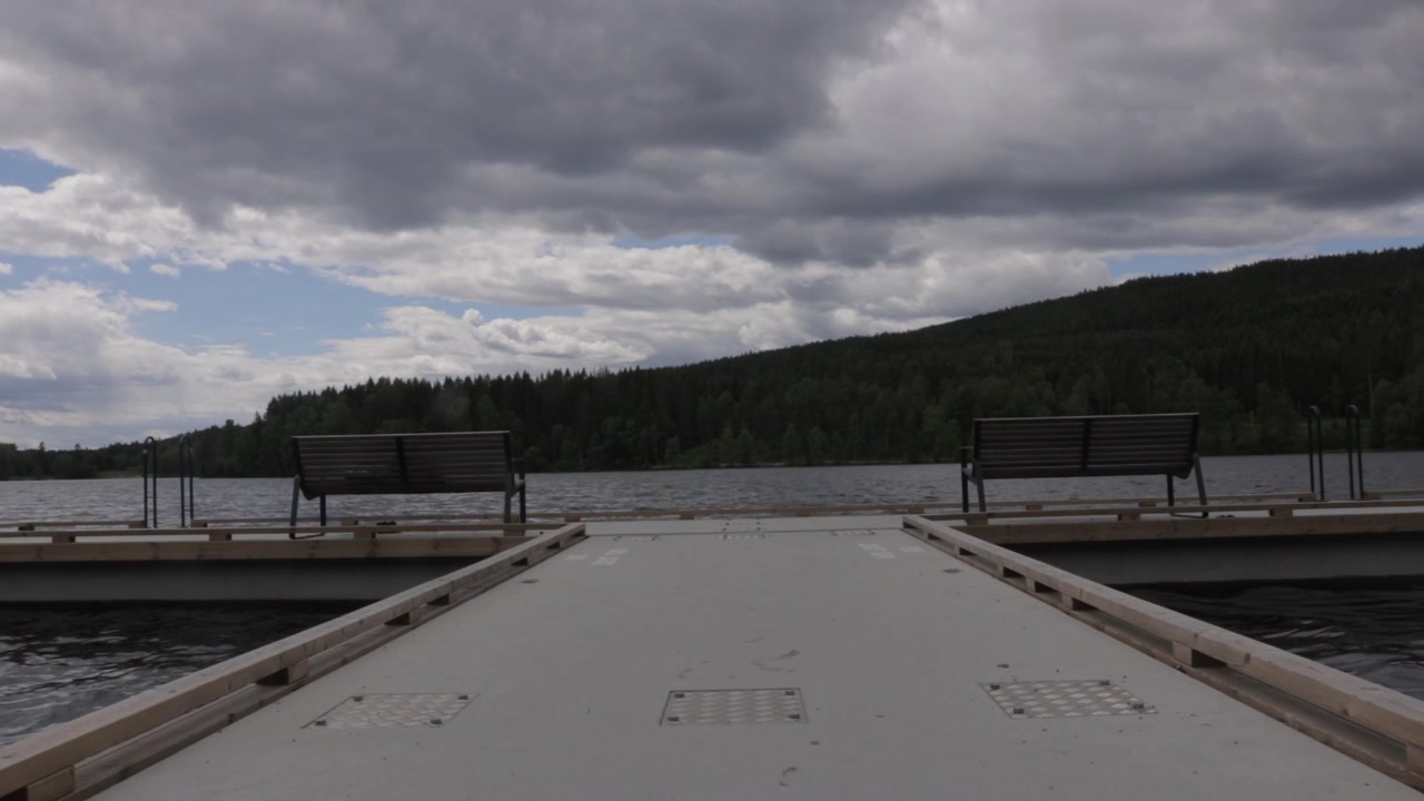 Symmetrical view of empty park benches on floating pier facing lake water
