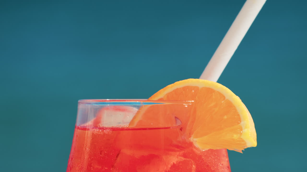 Close up of a refreshing red orange cocktail with orange slice and ice cubes, captured outdoors on a sunny day in Cannes