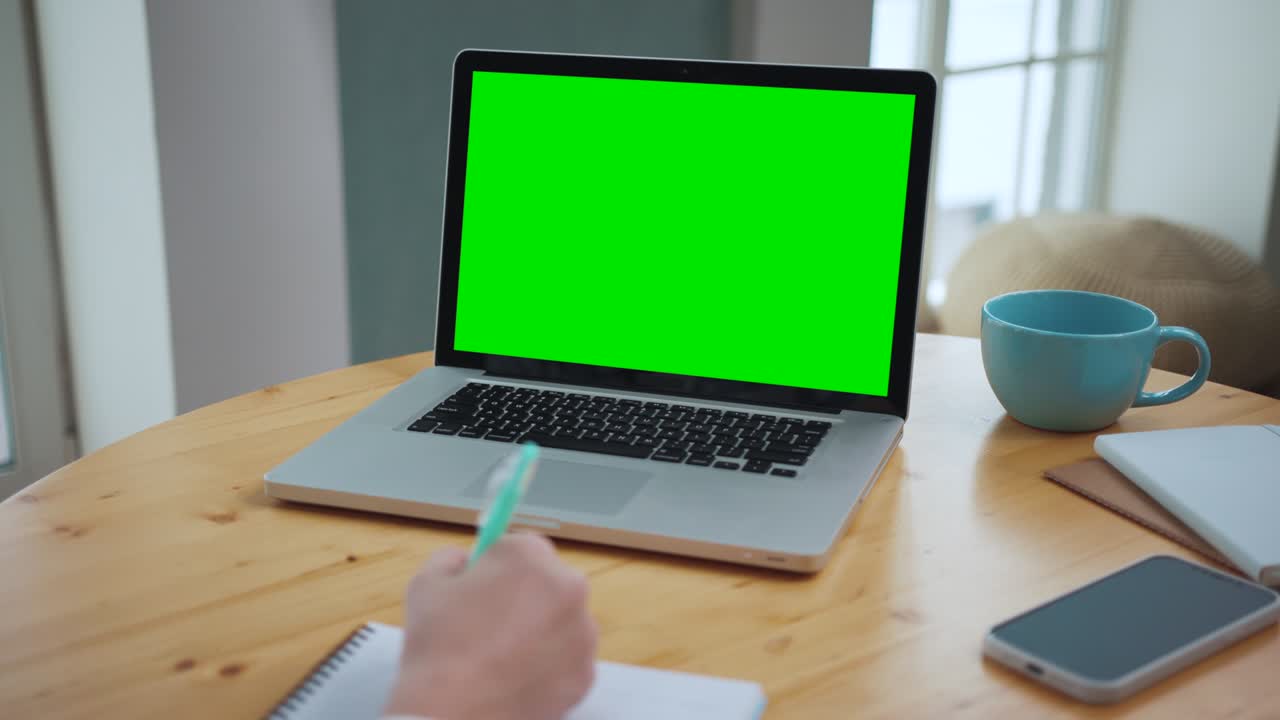 Man Looking at Green Screen on Work Laptop. Office Person Using Laptop Computer with Green Screen. Guy Study with Chroma Key Mockup in a Workplace Environment. Young Writing Note on Learning Lecture
