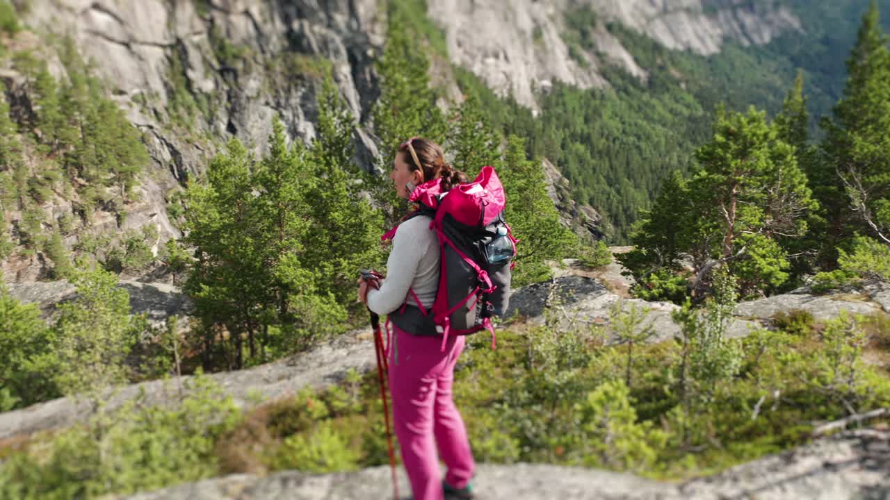 una excursionista parada en el afloramiento rocoso de la montaña disfrutando de la vista del amplio valle debajo después del largo y desafiante ascenso