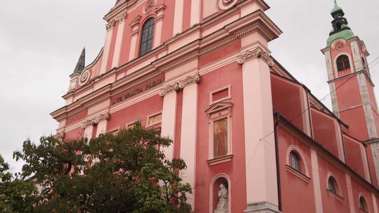 View of the Franciscan Church of the Annunciation in Ljubljana with its distinctive pink facade and bell tower.