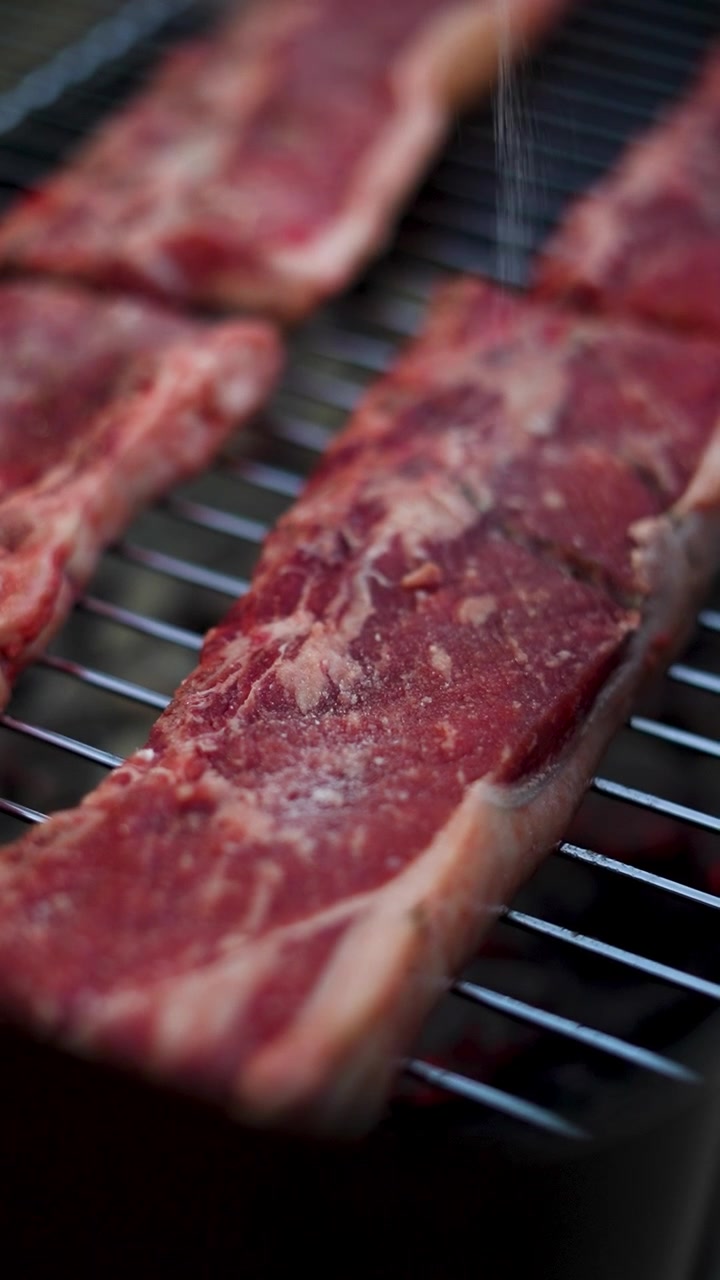 Vertical video of sprinkling salt on raw beef meat on a grill