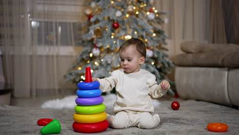 baby playing with stacking rings near christmas tree