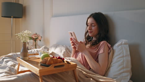 peaceful woman using smartphone in hotel room. calm female holding coffee cup