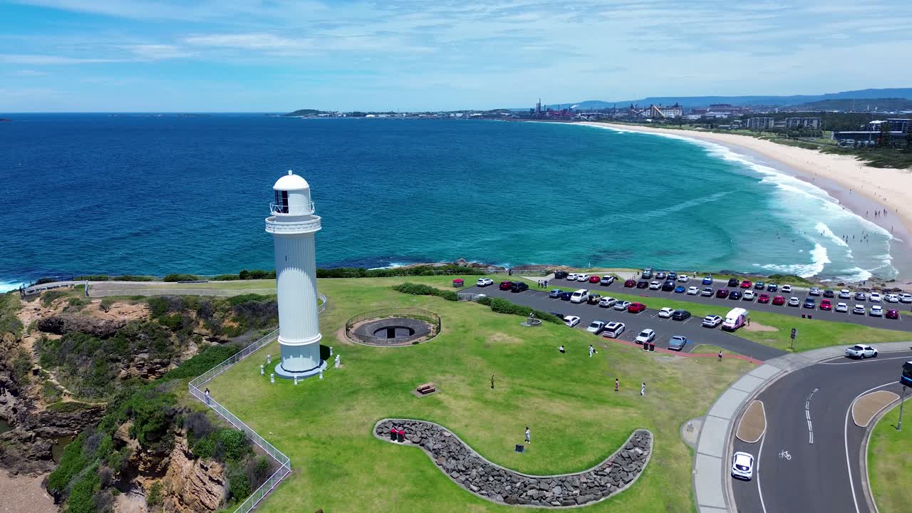 Drone aerial landscape of cars driving along main road near carpark at Flagstaff Point Lighthouse on headland hill with Wollongong ocean beach coastline in the background Illawarra Australia tourism