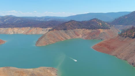 Inquietante-Antena-Sobre-El-Lago-Oroville-De-California-Asolado-Por-La-Sequía-Con-Bajos-Niveles-De-Agua,-Costa-En-Retroceso-Y-Barcos-En-Aguas-Bajas