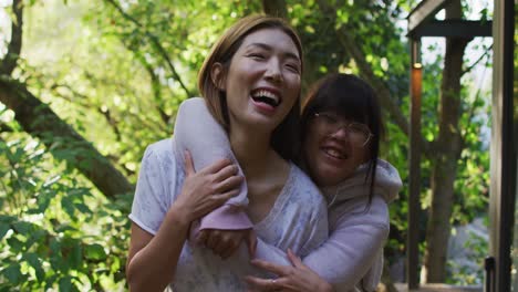 Portrait-of-asian-mother-and-daughter-embracing-in-garden-and-smiling