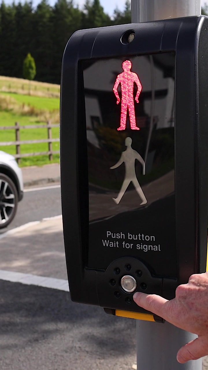A person presses a crosswalk button while a red pedestrian signal is illuminated outdoors.