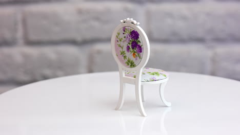 cute miniature wooden curved chair with flower print. toy piece of furniture rotating at white backdrop.