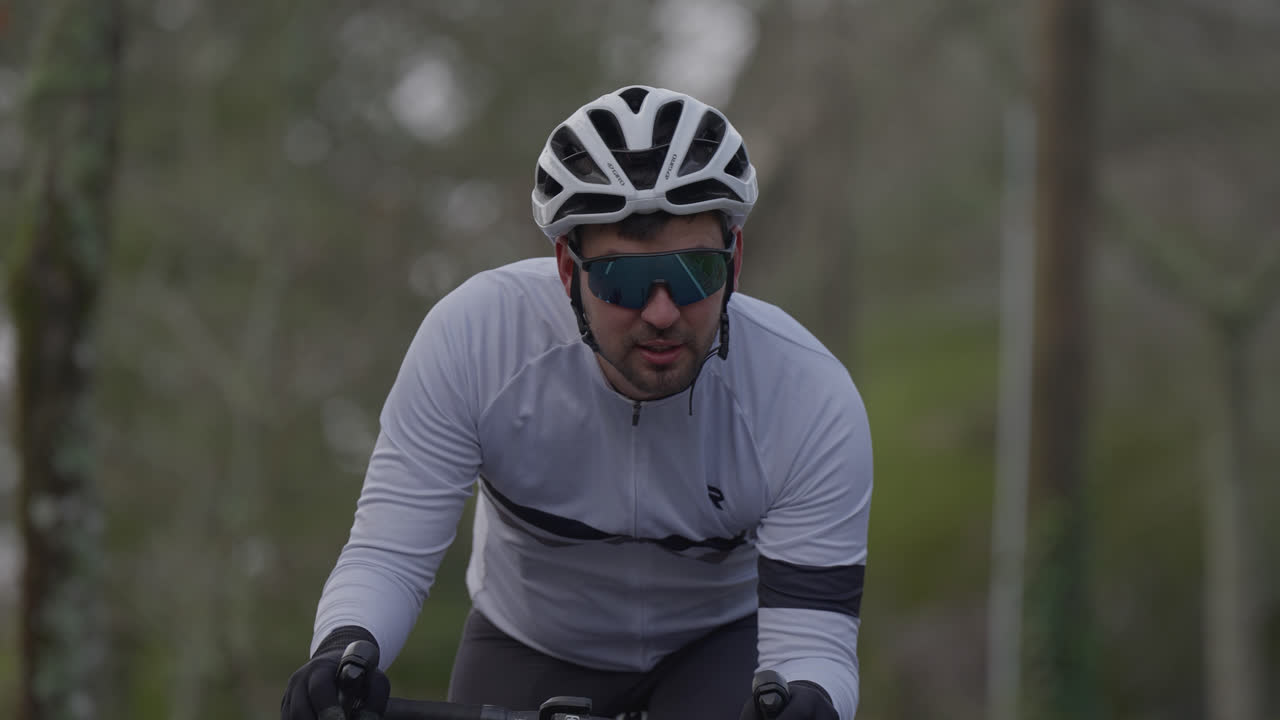 Uomo in bicicletta da corsa con casco, guanti e occhiali da sole su strada asfaltata.