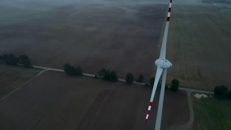 aerial close up of slow rotating wind turbine on brown farm field in nature - production of renewable energy during windless early morning in dawn