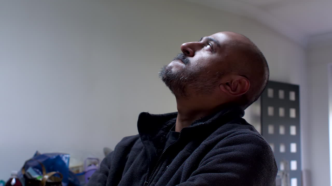 A man in an indoor setting paces back and forth, gazing at ceilings with a hint of worry and anxiety
